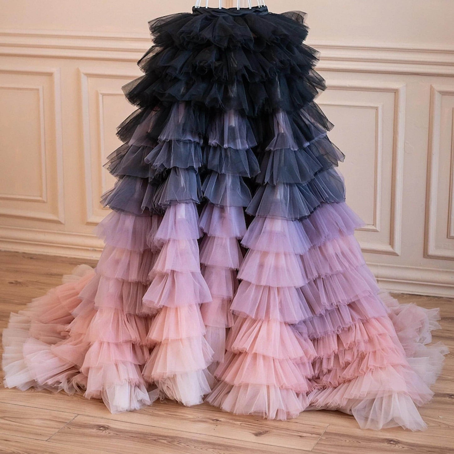 A long, voluminous, ruffled dress with a gradient of colors, transitioning from black to pink and purple.