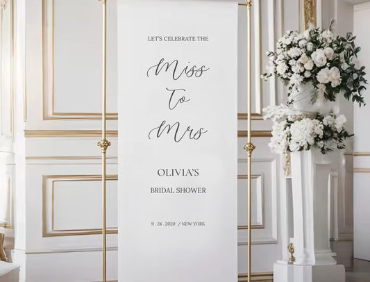 a white banner with black text that reads &quot;Let&#39;s celebrate the miss to mrs Olivia&#39;s bridal shower 9. 24. 2020 / NEW YORK&quot;.