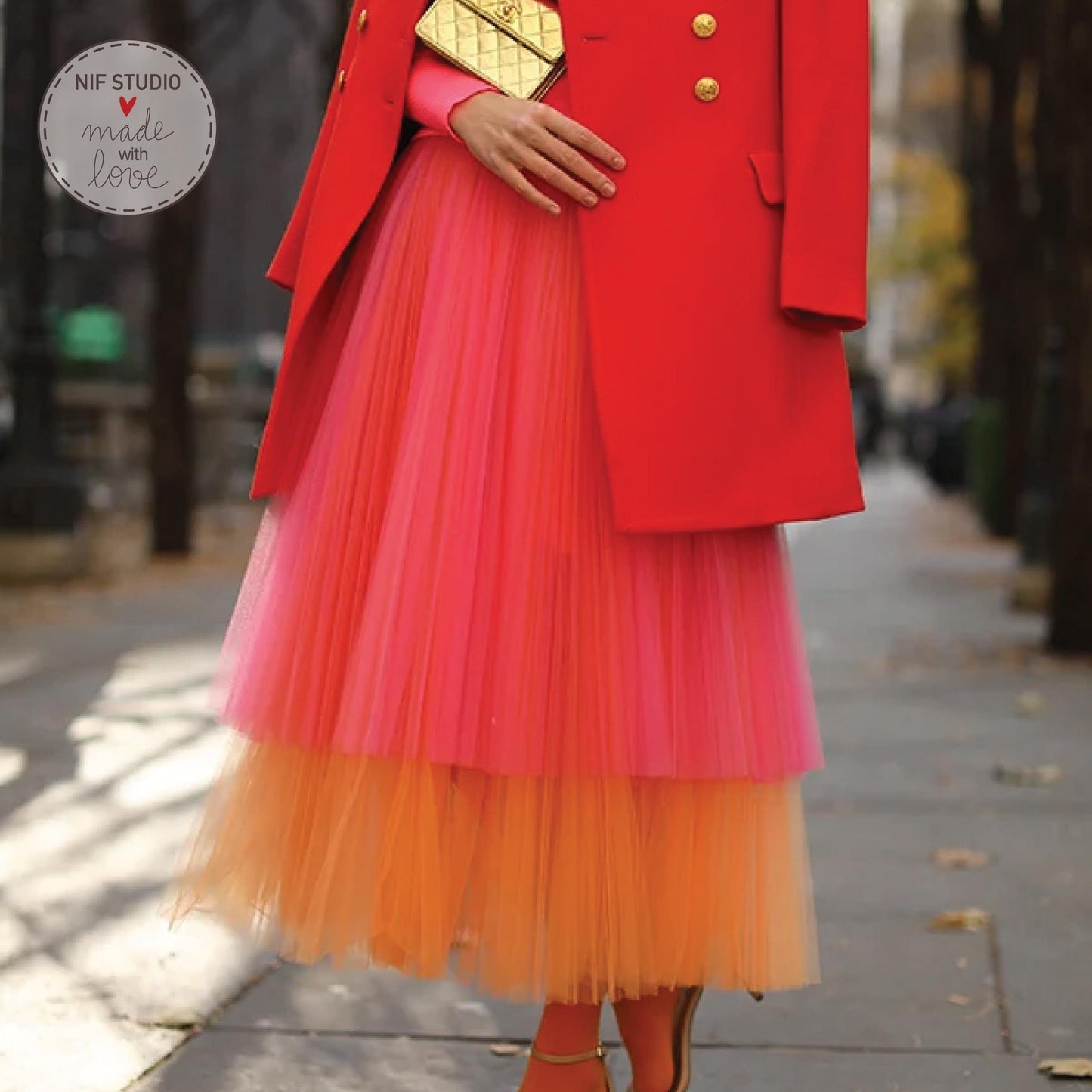 A woman wearing a red coat and a pink and orange tulle skirt is walking on a sidewalk.