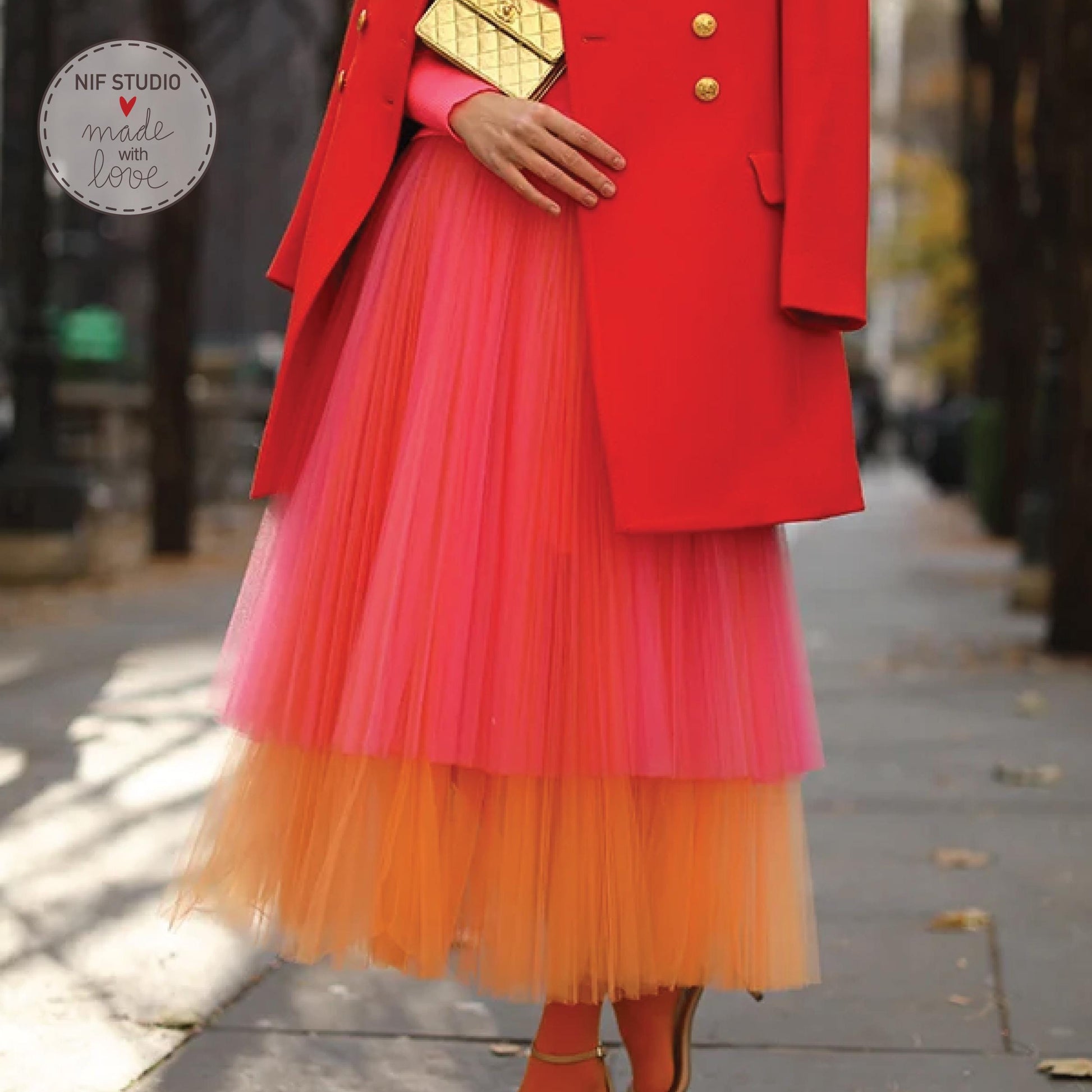 A woman wearing a red coat and a pink and orange tulle skirt is walking on a sidewalk.