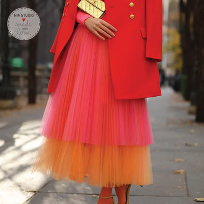 A woman wearing a red coat and a pink and orange tulle skirt is walking on a sidewalk.