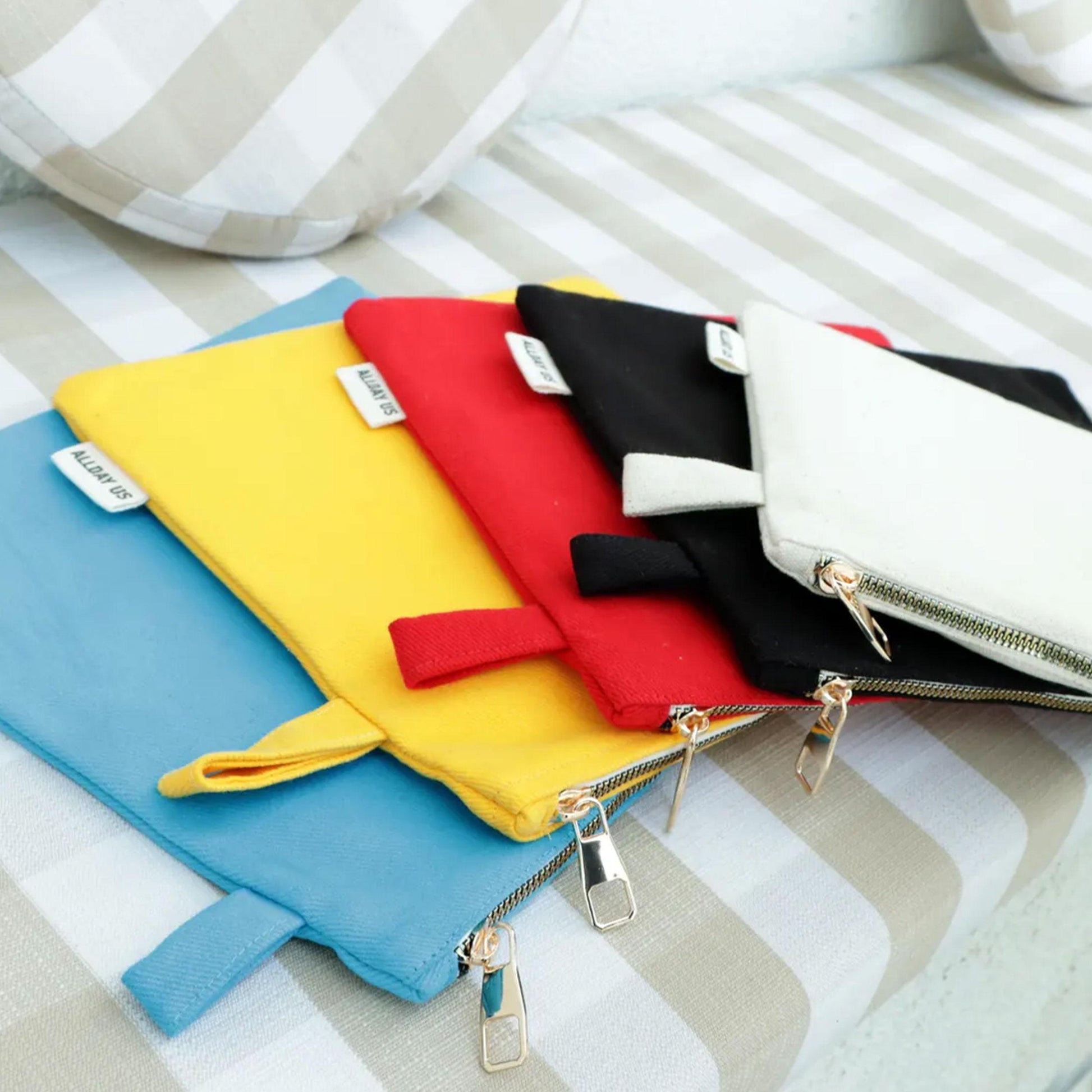 A collection of colorful tote bags with zippers, arranged on a striped surface.