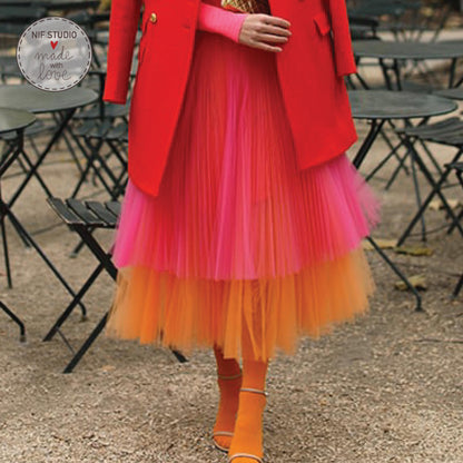 A woman wearing a red coat and a colorful tulle skirt is walking on a gravel path.