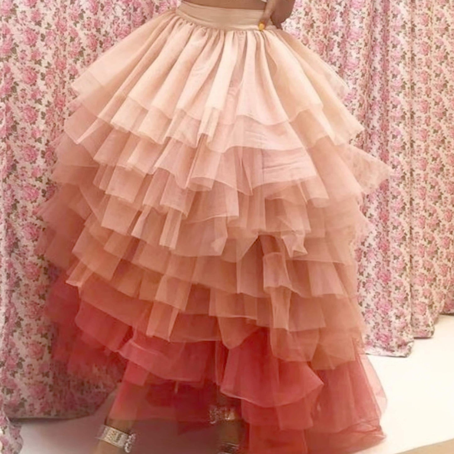 A woman wearing a long, ruffled skirt with a gradient of pink and orange colors.
