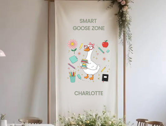 a banner with a cartoon goose holding books and other school supplies, surrounded by flowers and greenery.