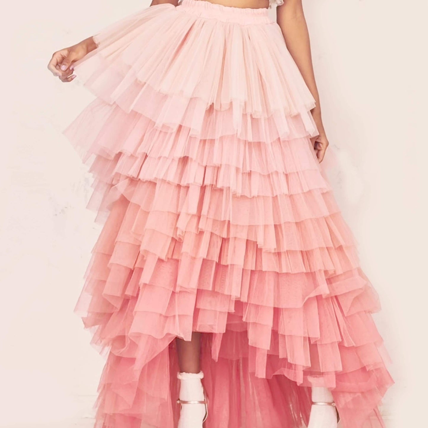 A woman wearing a long, ruffled pink and white tulle skirt with a high slit.