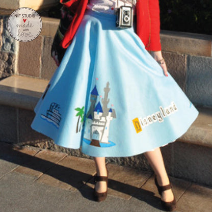 A woman wearing a blue skirt with a castle and palm tree design, standing on a stone walkway.