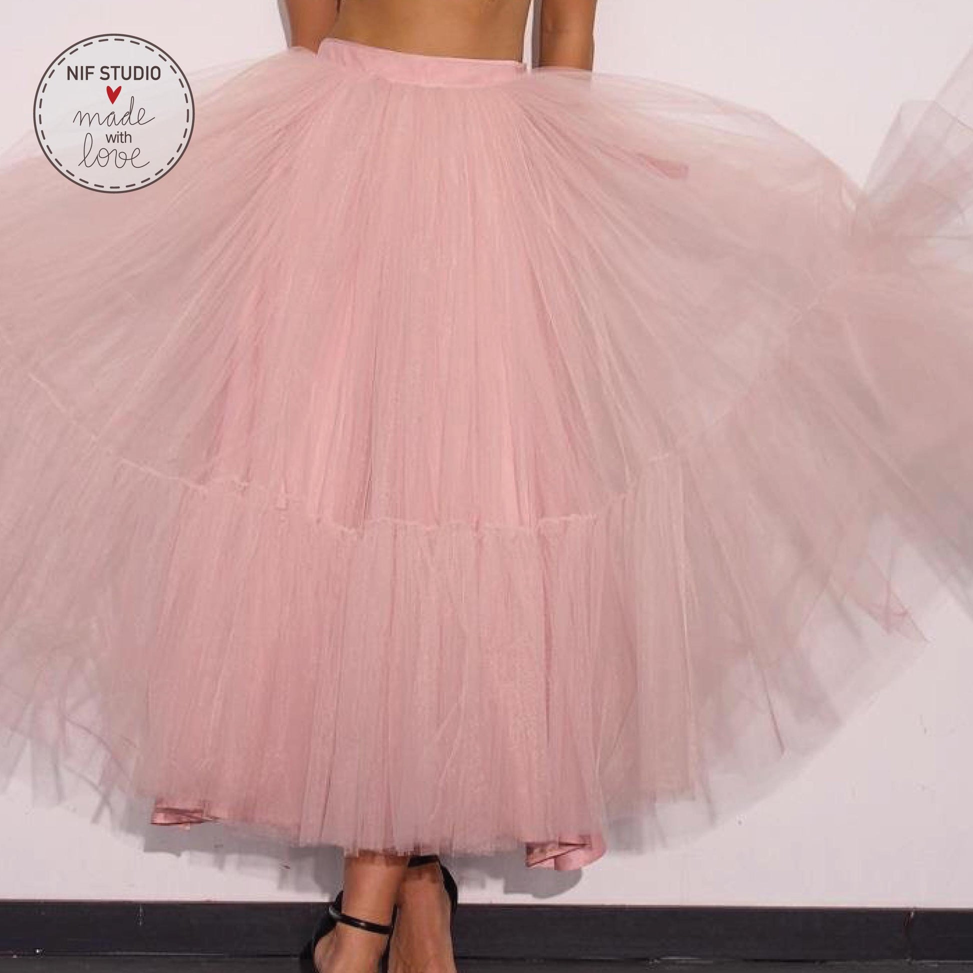 A woman wearing a large, flowing pink tulle skirt stands against a white background.