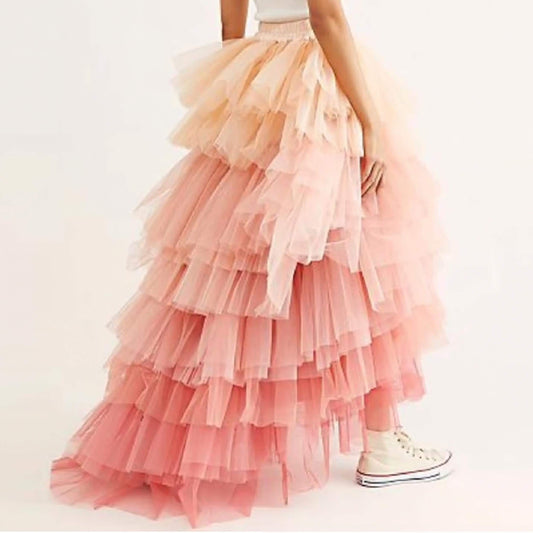 A person wearing a long, ruffled pink and peach tulle skirt with a high slit, paired with white sneakers.