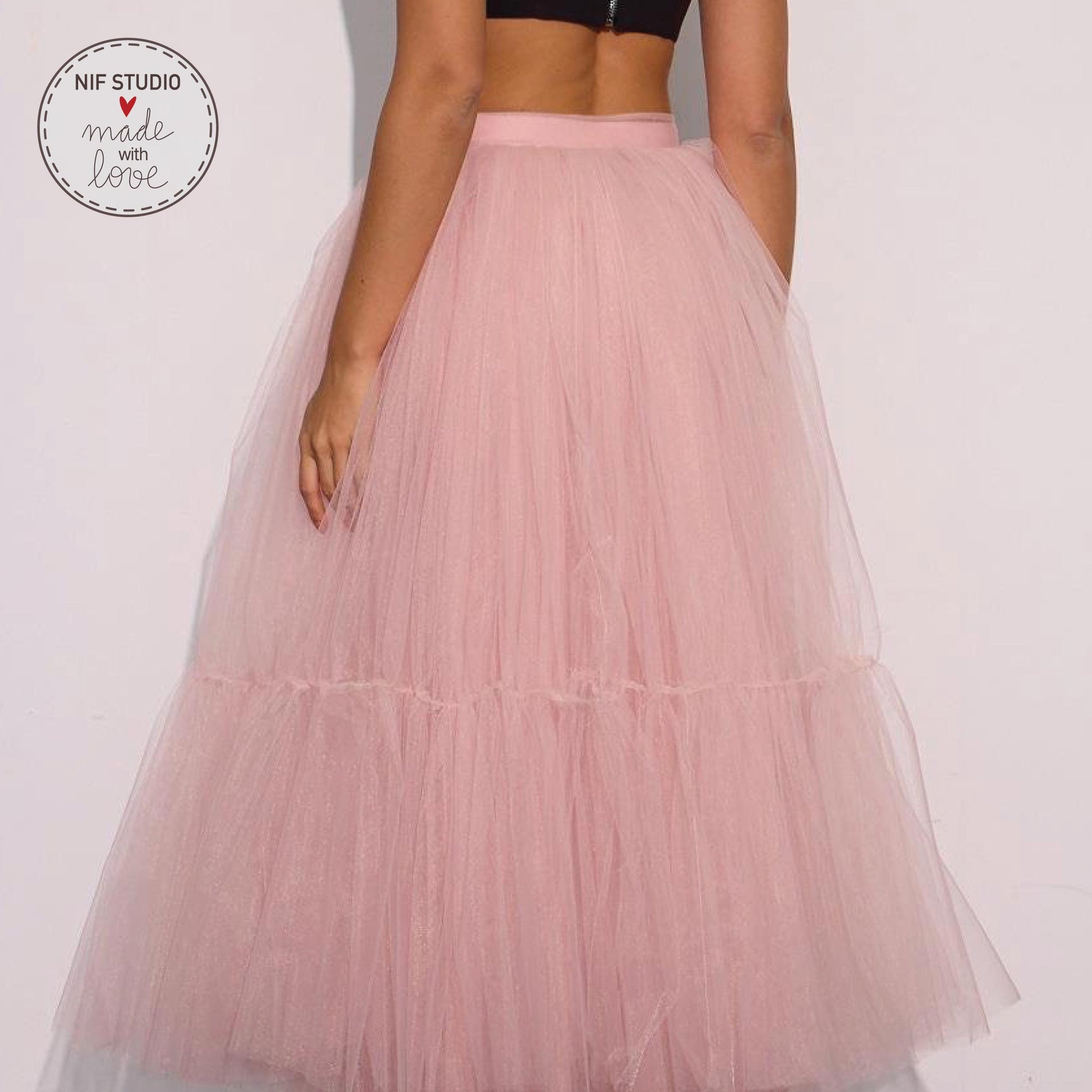 A woman wearing a pink tulle skirt stands against a white background.