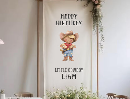 A banner with a cartoon cowboy character and the text &quot;Happy Birthday Little Cowboy Liam&quot; hanging on a wall.