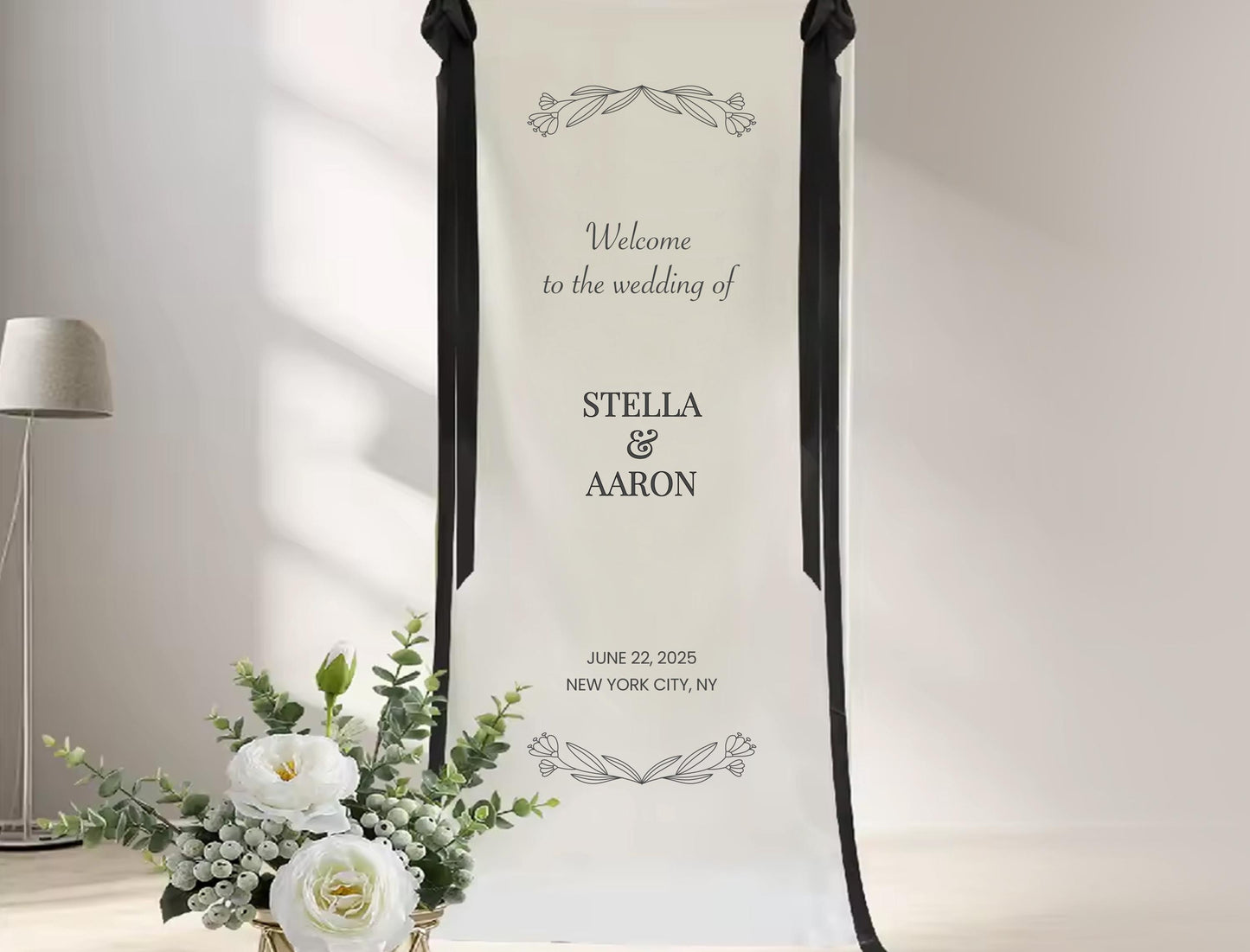 a wedding invitation banner with the names &#39;Stella & Aaron&#39; and the date &#39;June 22, 2015&#39; in New York City, New York. The banner is displayed in front of a floral arrangement, and there is a lamp visible in the background.